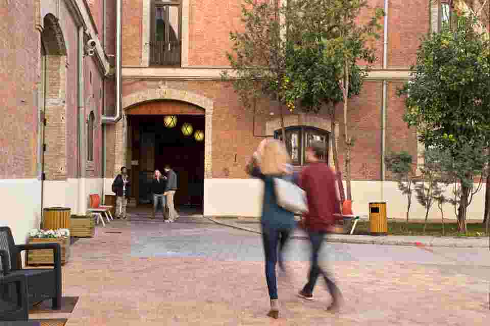 Un grupo de personas camina por un patio con arquitectura de ladrillo y árboles.