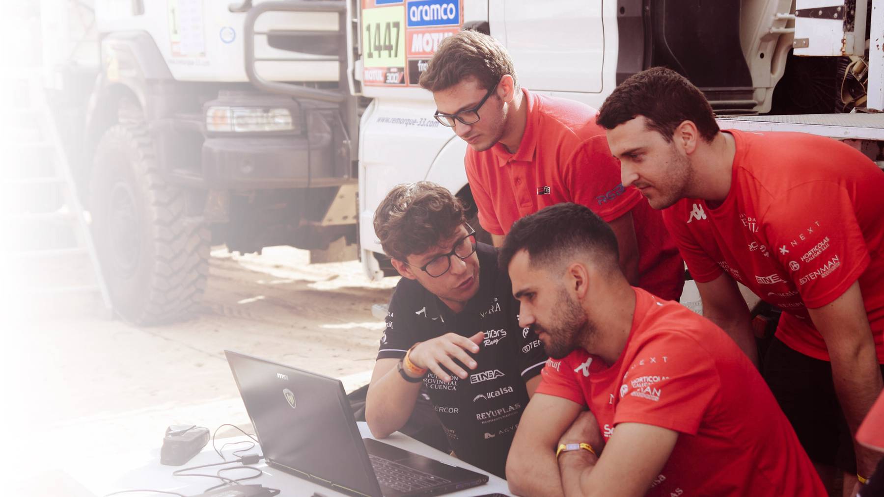 Cuatro personas observan atentamente una computadora portátil en un ambiente de trabajo relacionado con vehículos.