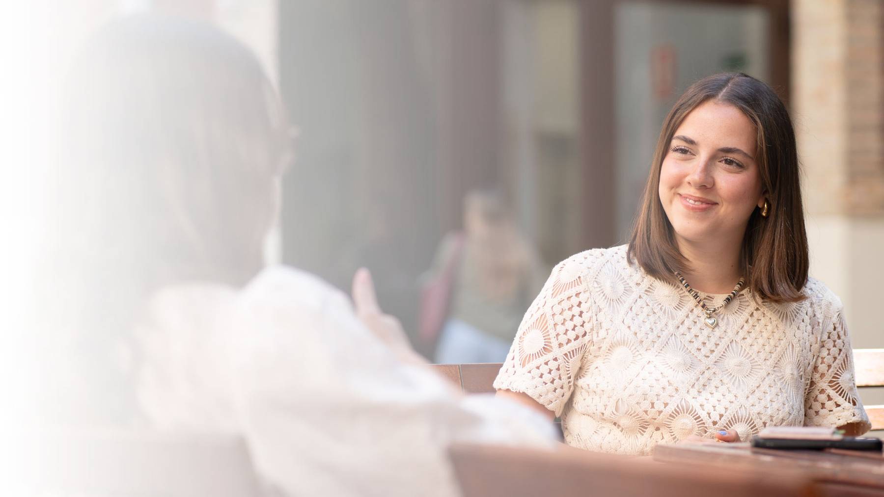 Una mujer sonriente sentada en una mesa, conversando de manera amigable.