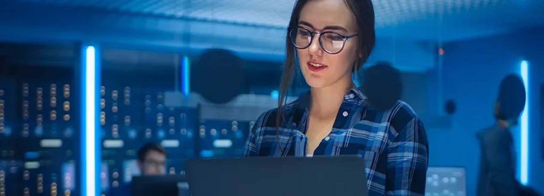 Una mujer con gafas utiliza un portátil en un entorno tecnológico iluminado con luces azules.