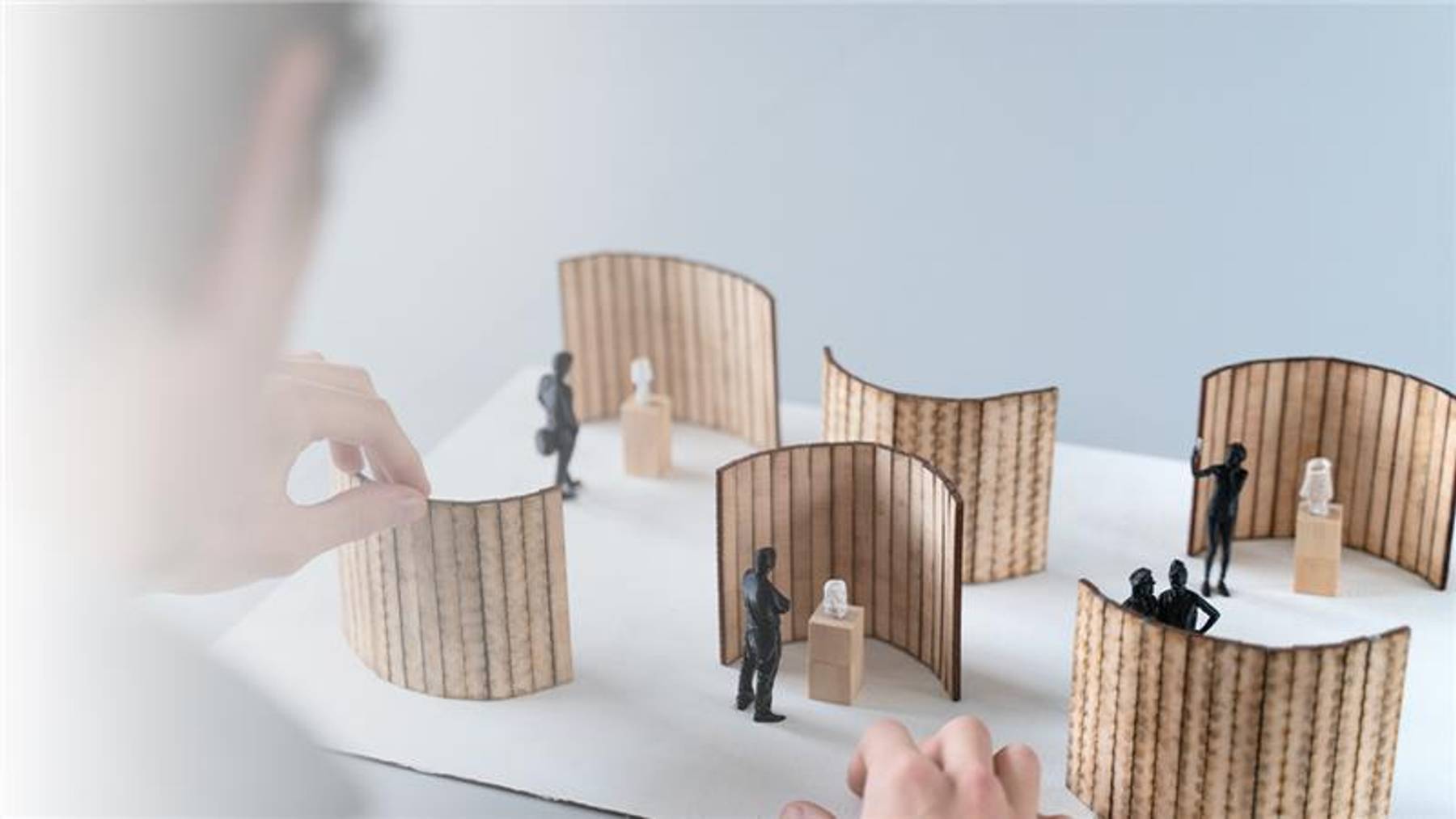 Una persona está ajustando unos paneles en una maqueta de una exhibición con figuras en miniatura.