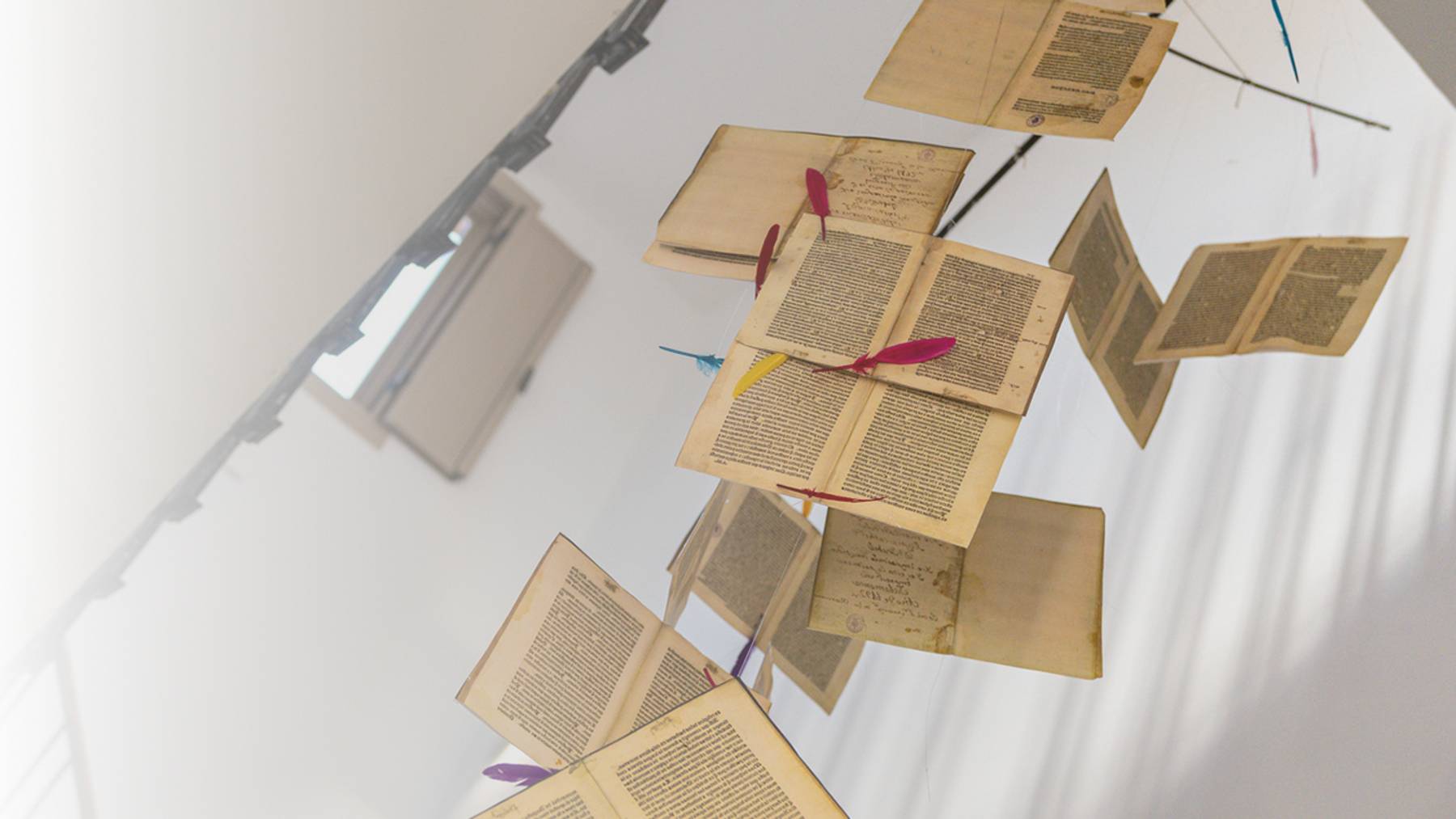 Una serie de libros flotantes con plumas de colores en el medio de un espacio iluminado.