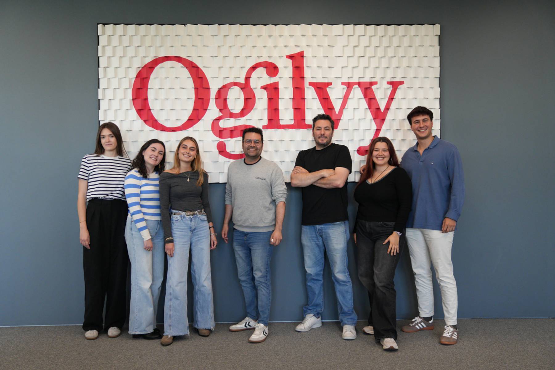 Un grupo de ocho personas posando frente a un mural con el nombre 'Ogilvy'.
