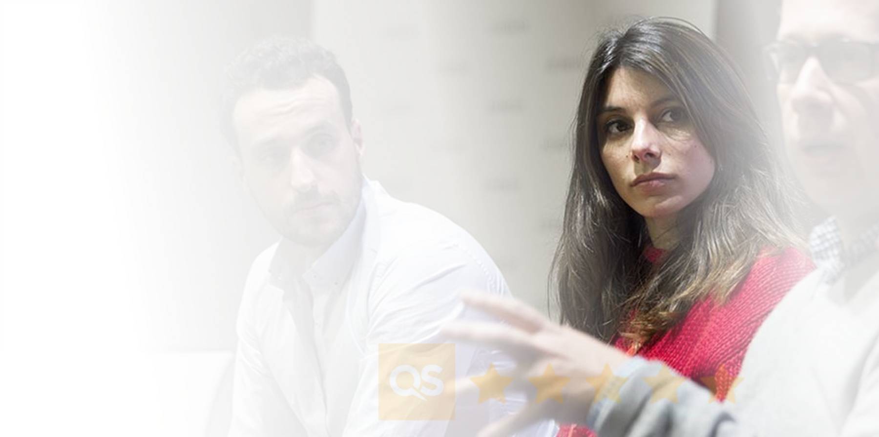 Una mujer con cabello largo y oscuro escucha atentamente mientras un hombre habla en un entorno de discusión.