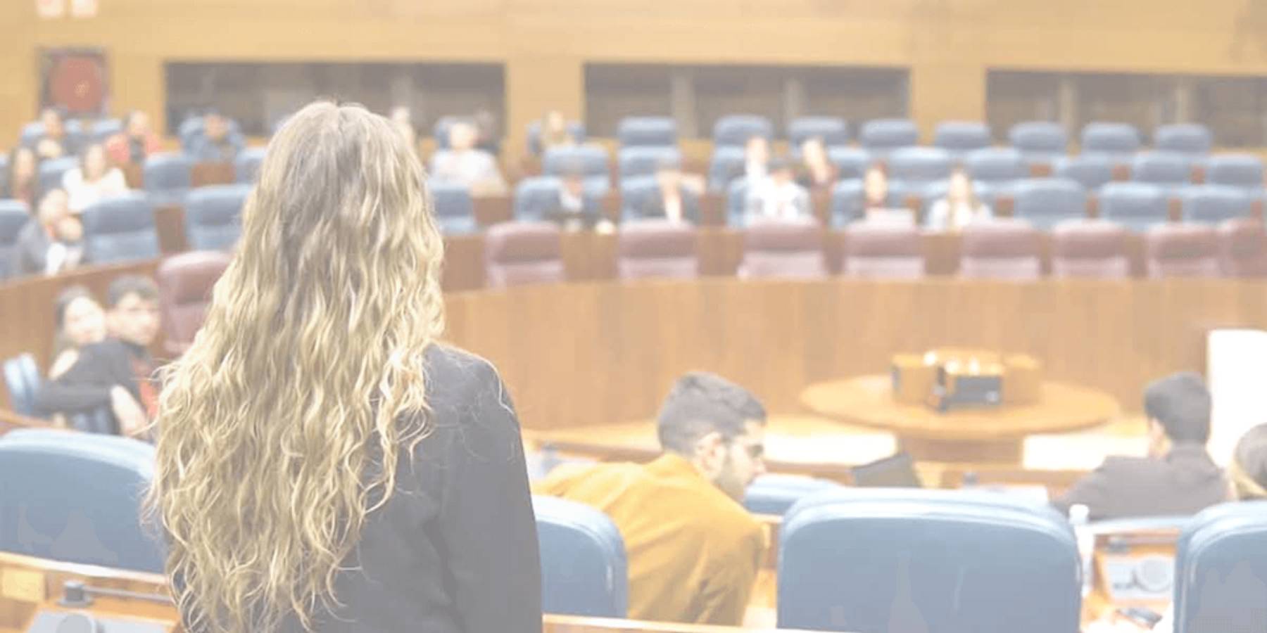 Una mujer con el cabello rizado de pie en un auditorio vacío durante una sesión legislativa.
