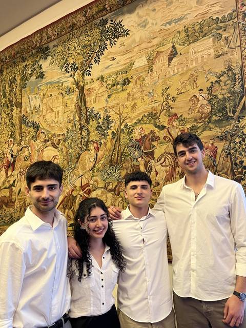 Un grupo de cuatro personas se posan sonrientes frente a un tapiz histórico en un entorno interior.