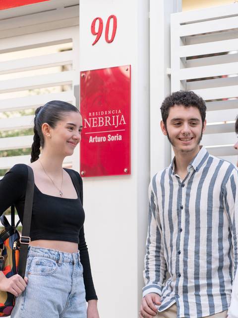 Tres jóvenes conversan frente a un edificio que parece ser una residencia estudiantil.