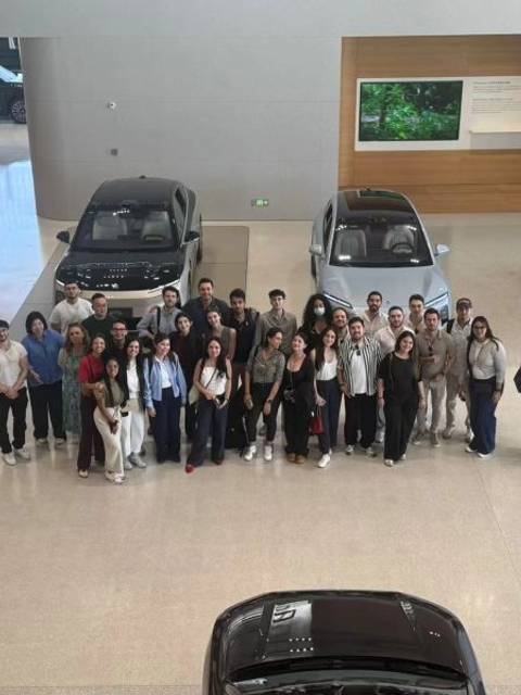 Grupo de personas posando frente a varios automóviles en un recinto moderno.