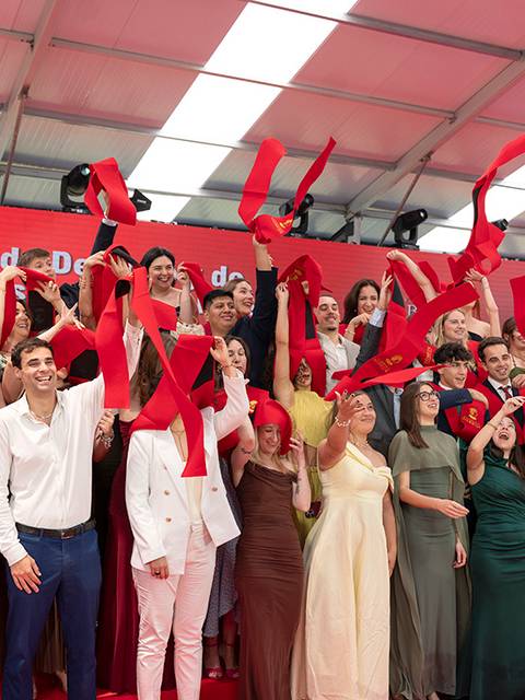 Grupo de graduados celebrando con bandas rojas en una ceremonia de entrega de diplomas.