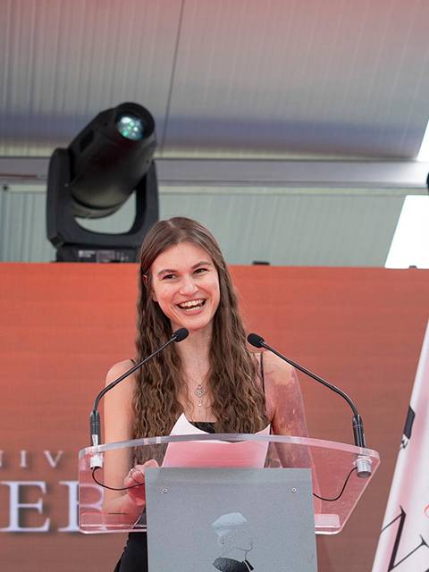 Una joven sonriente habla en un podio durante un evento en la Universidad de Nebraska.