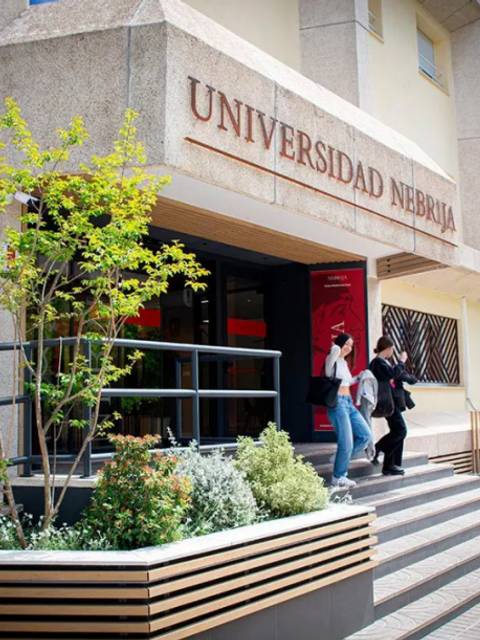 La imagen muestra la entrada de la Universidad Nebrija con estudiantes entrando al edificio.
