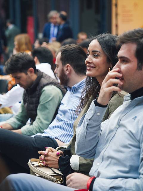 Un grupo de personas sentadas en un evento, mostrando diversas expresiones mientras escuchan.