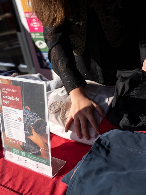 Una persona organiza ropa sobre una mesa junto a un cartel de recolección de ropa.