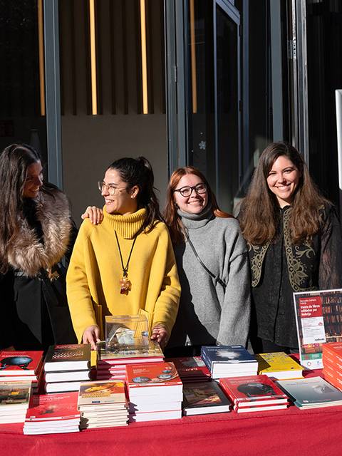 Una grupo de cinco mujeres sonríen detrás de una mesa llena de libros en un evento al aire libre.