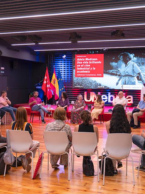 Una reunión en un auditorio con varias personas sentadas en círculo y una presentación en pantalla.