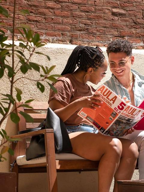 Una pareja sonriente contempla un folleto mientras se relajan en un sofá al aire libre.