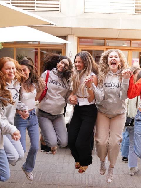 Un grupo de mujeres sonrientes saltando juntas en un ambiente festivo al aire libre.
