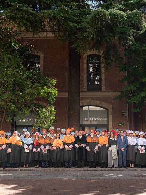 Grupo de personas uniformadas posando frente a un edificio con árboles alrededor.