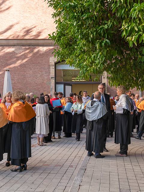Un grupo de personas vestidas con togas conversando en un espacio al aire libre.