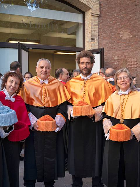Un grupo de personas vestidas con togas y birretes de diferentes colores en un acto académico.