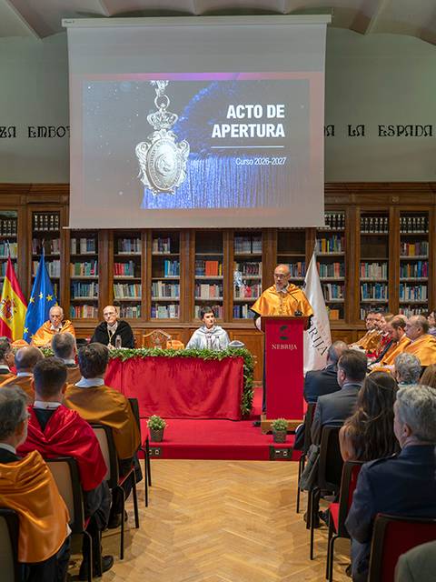 El acto de apertura se celebra en una biblioteca con un gran número de asistentes y un ponente en el escenario.