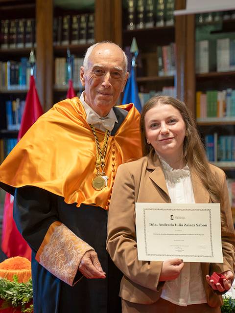 La imagen muestra a un académico entregando un diploma a una estudiante en un acto de graduación.