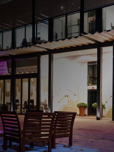 Una fachada moderna con sillas de madera en un ambiente nocturno y luces de colores.