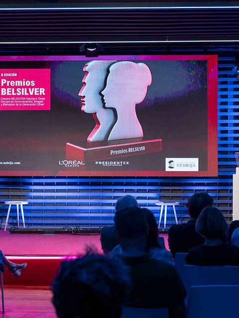 Un evento de entrega de premios con un presentador y una pantalla de fondo que muestra el título 'Premios BELSILVER'.