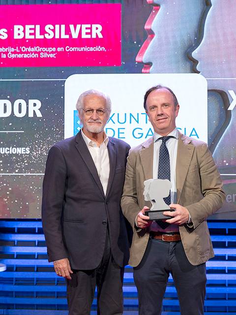 La imagen muestra a dos hombres en una ceremonia de premiación, uno de ellos sosteniendo un trofeo.