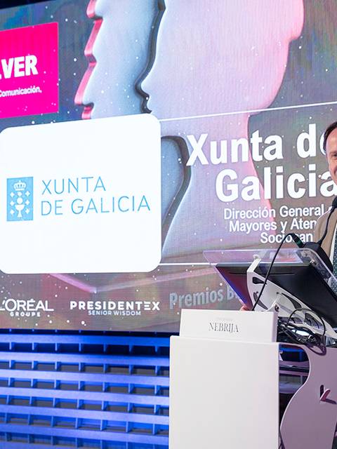 Un hombre presenta premios en un evento relacionado con la comunicación y el marketing en un escenario iluminado.
