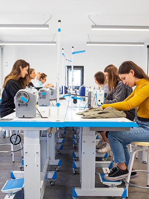 Un grupo de mujeres jóvenes trabaja en máquinas de coser en un taller de costura.