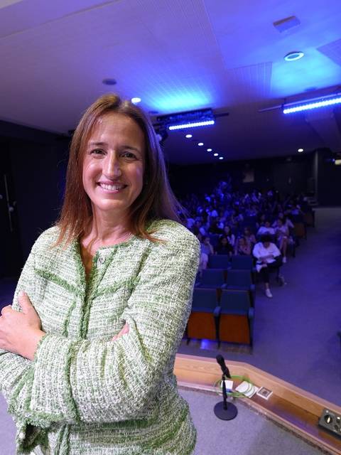 Una mujer sonriente en un escenario frente a un público en un auditorio.
