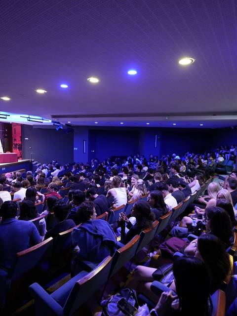Una gran multitud de personas sentadas en un auditorio, asistiendo a un evento con luces de colores.