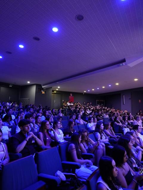 Una multitud de personas observa un evento en un auditorio iluminado con luces azules.