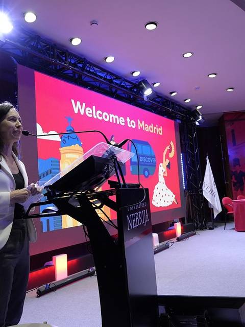 Una mujer da un discurso en un evento en Madrid, con una presentación de fondo que dice 'Welcome to Madrid'.