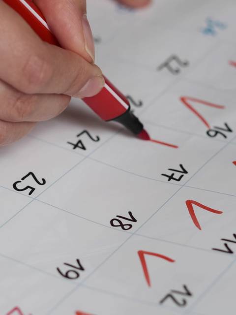Una mano escribe en un calendario con un bolígrafo rojo.
