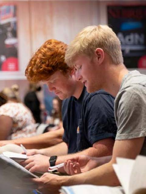 Dos jóvenes estudiando y leyendo en un ambiente académico.