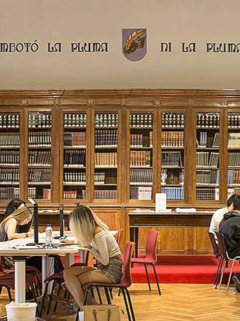 Una biblioteca con estanterías llenas de libros y personas estudiando en mesas.