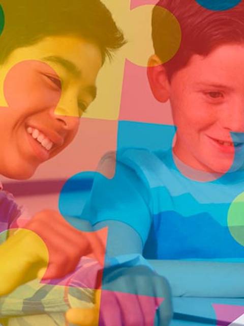 Dos niños sonríen mientras juegan con piezas de un rompecabezas colorido.