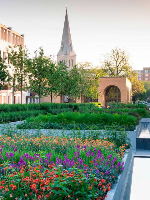 Un hermoso jardín urbano lleno de flores coloridas con un fondo de edificios y una iglesia de aguja alta.