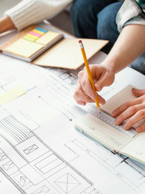 Dos personas trabajan en un plano sobre una mesa, tomando notas y haciendo anotaciones.