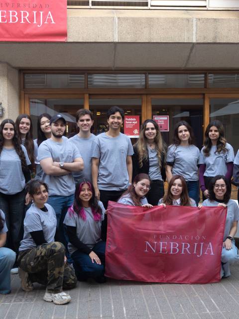 Grupo de estudiantes posando juntos con camisetas grises y una bandera de la universidad Nebrija.