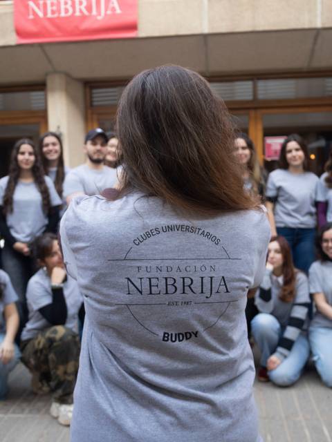 Un grupo de estudiantes posa frente a un edificio, con camisetas grises que tienen el logo de la Fundación Nebrija.