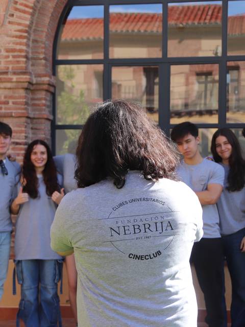 Un grupo de estudiantes posando al aire libre con camisetas grises frente a un edificio.