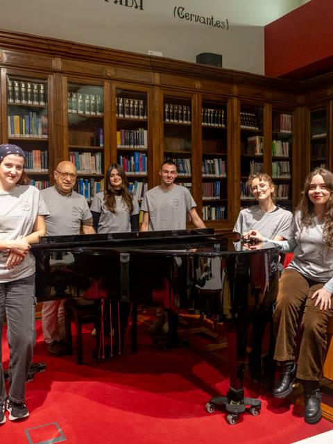 Un grupo de personas sonríen frente a un piano en un ambiente educativo y musical.