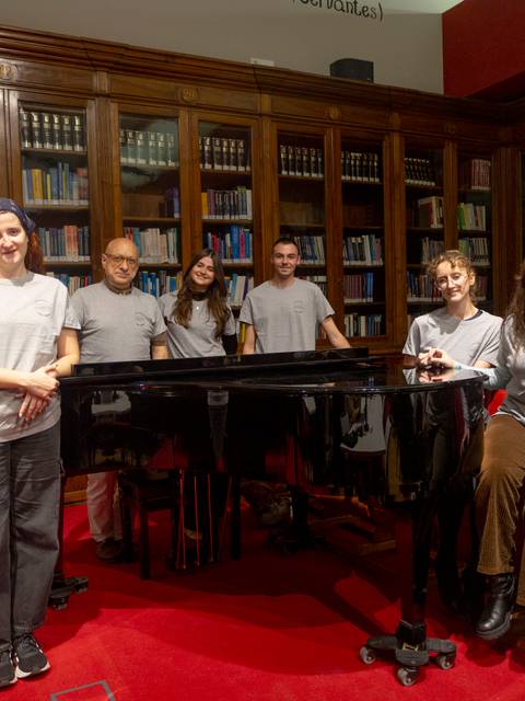 Grupo de personas posa junto a un piano en una sala con estanterías de libros.