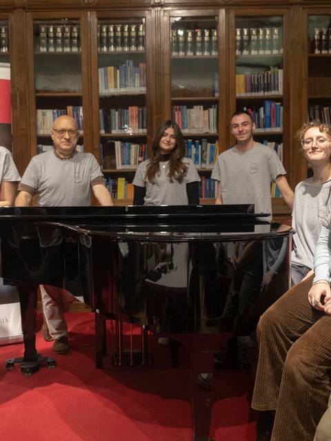 Un grupo de personas sonrientes se encuentra frente a un piano en una biblioteca.