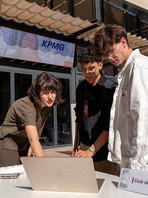 Un grupo de tres jóvenes interactúa frente a una computadora portátil en un ambiente al aire libre.