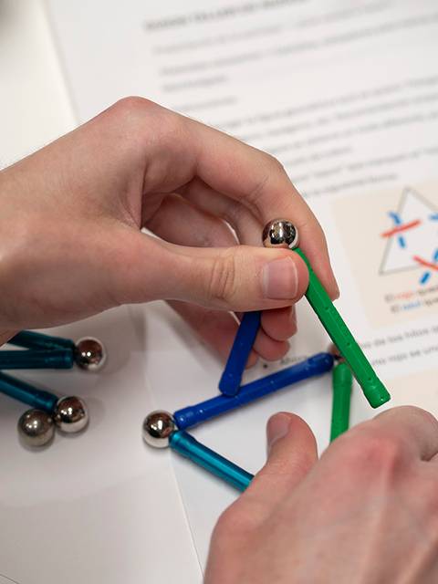 Una persona está manipulando un modelo con piezas de colores en una mesa junto a un documento impreso.