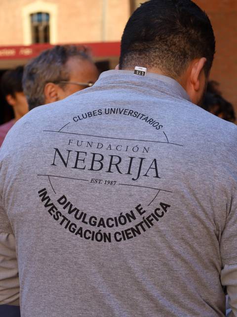Una persona de espaldas lleva una camiseta gris con el logo de la Fundación Nebrija.